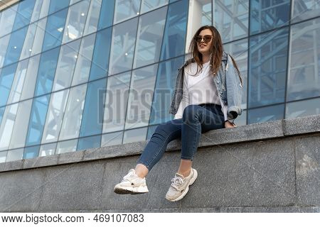 Smiling Stylish Woman Resting On City Street. Young Woman In Sunglesses In Youth Clothing On The Cit
