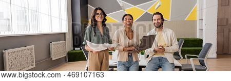 Cheerful Multicultural Business Colleagues With Documents And Gadgets Looking At Camera In Modern Of