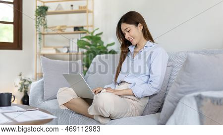 Woman using laptop to work or do homework at home with smiling face in her living room, Creating hap