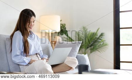Woman using laptop to work or do homework at home with smiling face in her living room, Creating hap