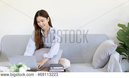 Woman using laptop to work or do homework at home with smiling face in her living room, Creating hap