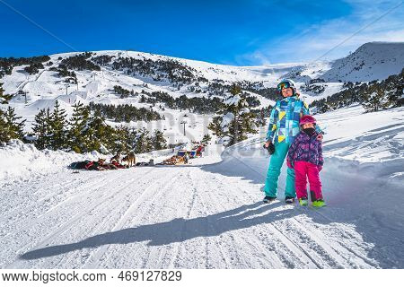 Mother And Daughter, Skiers, Standing On Snowy Road, Huskey Dog Sledding, Mountains And Forest In Ba