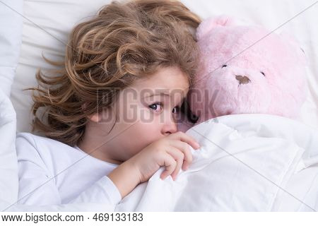 Child Wakes Up With Toy Teddy Bear In The Morning In The Bedroom. Cute Little Boy Waking Up In Bed.