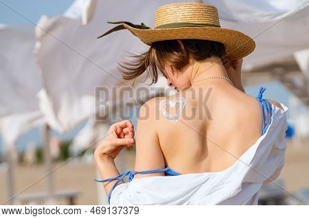 Young Woman In Straw Sunhat With Sun Cream On Tanned Back In Form Heartlet, Shape Heart. Skincare. C