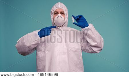 A Male Doctor In Protective Overalls And A Mask Pointing At Ampoule With A Vaccine In His Hands. Cor