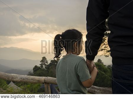 Father Holding Daughter's Hand, They're Stand And Look At The Beautiful Scenery Of The Sunset At The