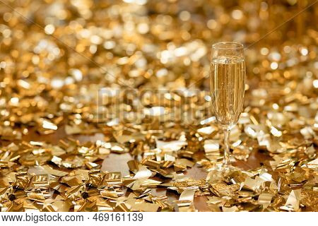 A Glass Of Champagne Stands In Front Of Piles Of Golden Coffee On The Floor. Holiday Concept. Place 