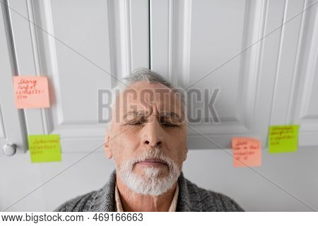 Depressed Man Suffering From Azheimers Syndrome Standing With Closed Eyes In Kitchen.
