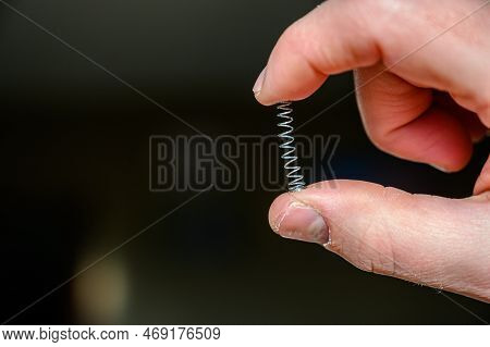 Caucasian Hand Compressing A Metal Spring Between A Thumb And Finger