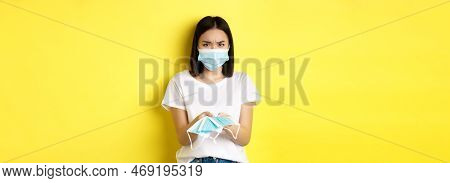 Coronavirus, Quarantine And Medicine Concept. Angry Asian Girl Giving You Medical Mask Indoors, Frow