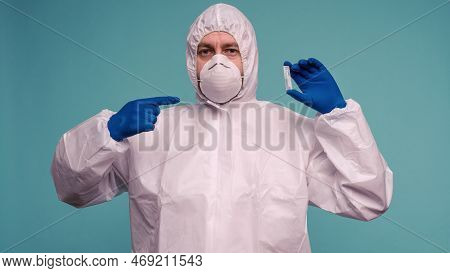 A Male Doctor In Protective Overalls And A Mask Pointing At Ampoule With A Vaccine In His Hands. Cor
