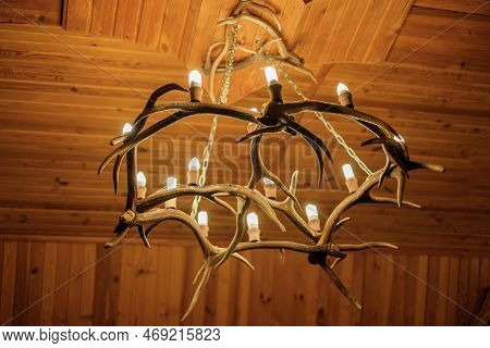 Chandelier On The Ceiling Made Of Deer Antlers. A Light Bulb In The Shape Of A Candle.