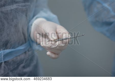 The Surgeon Holds A Volkmann Spoon In An Outstretched Hand In A Medical Glove Against The Background