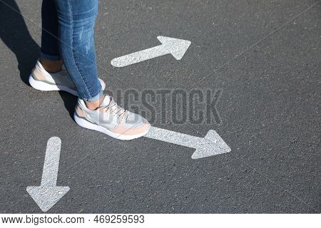 Choice Of Way. Woman Walking To Drawn Mark On Road, Closeup. White Arrows Pointing In Different Dire