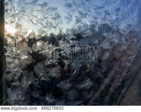 Frosty Patterns On The Window Glass. The Patterns Are Like Light Feathers. Trees Are Visible Through