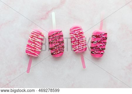 Homemade Decorated Cakesicles For Valentines Day, On A Pink Marble Surface.