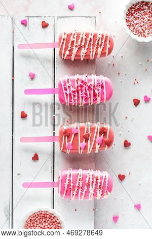 Valentines Day Cakesicles On A Rustic Wooden Board With Sprinkles All Around.