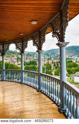 Carved Wooden Balcony With View To Rike Park, Hills And Colorful Buildings In Historical Tbilisi, Ge