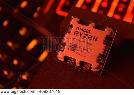A Close-up Of An Amd Ryzen 9 3900X Processor In A Packaging Box With Backlit Keyboards In The Backgr