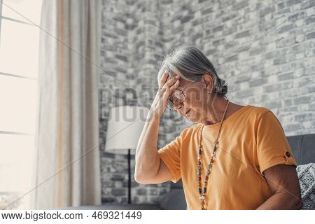 Sad Depressed Middle Aged Mature Woman Sitting Alone At Home Touching Head Feeling Headache Migraine
