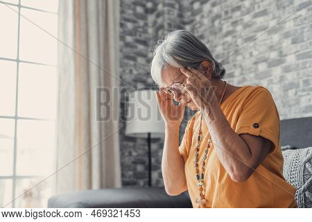 Sad Depressed Middle Aged Mature Woman Sitting Alone At Home Touching Head Feeling Headache Migraine