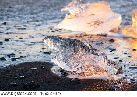Diamond Beach In Iceland. Icebergs Shining On Black Volcanic Sand At Sunset. Clear Ice Crashed By Oc