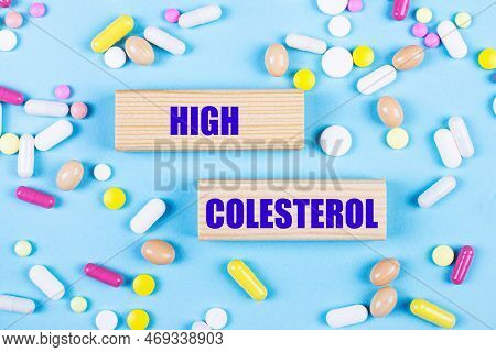On A Light Blue Background, Multi-colored Pills And Wooden Blocks With The Text High Colesterol. Pha