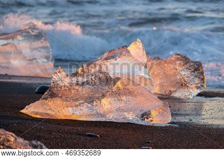 Diamond Beach In Iceland. Icebergs Shining On Black Volcanic Sand At Sunset. Clear Ice Crashed By Oc