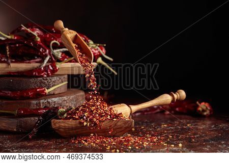 Chilli Flakes Are Poured Into A Wooden Dish. Chilli Flakes And Dried Chili Peppers On A Brown Backgr