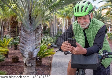 Portrait Of A Handsome Senior Man Using Smart Phone While Bike Ride In Outdoor Tropical Place. White