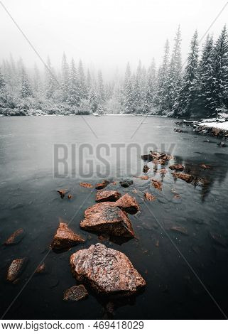Vertical Photo Of Peaceful And Tranquil Frozen Lake With Stones On The Surface In Winter Time. Snow 