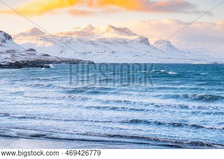 Icelandic Fjords During Sunset. Ocean Coast With Snowy Mountains And Orange Clouds. Winter Landscape