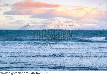 Icelandic Fjords During Sunset. Ocean Coast With Snowy Mountains And Orange Clouds. Winter Landscape