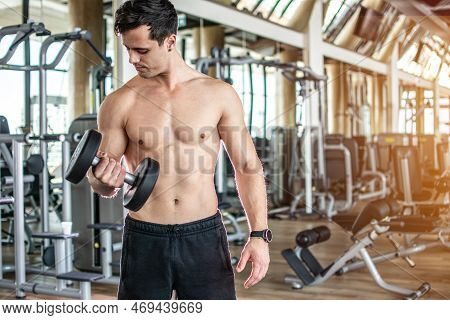 Young Man Lifting Dumbbell And Working Out On His Biceps At Gym.
