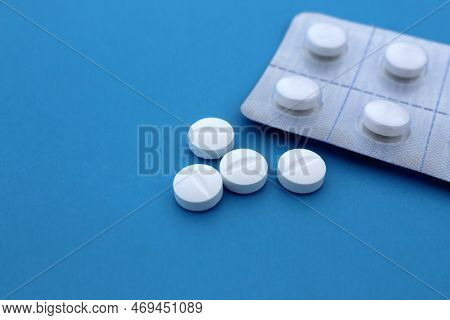 A Pile Of White Pills Lie On A Blue Background.