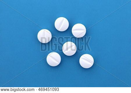 A Pile Of White Pills Lie On A Blue Background.