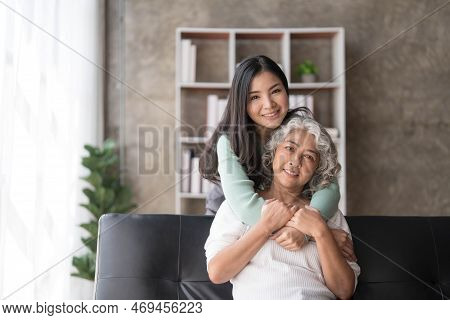 Loving Adult Daughter Hugging Older Mother, Standing Behind Couch At Home, Family Enjoying Tender Mo