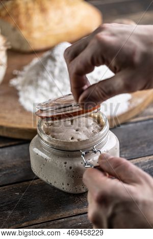 Male Hands Open A Jar With Active Yeast, Flour And Fresh Bread And Pastries In The Background