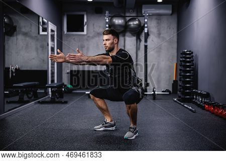 Leg Exercise, Using New Ems Technology. A Young Attractive Man In Ems Clothes In The Gym Doing Squat