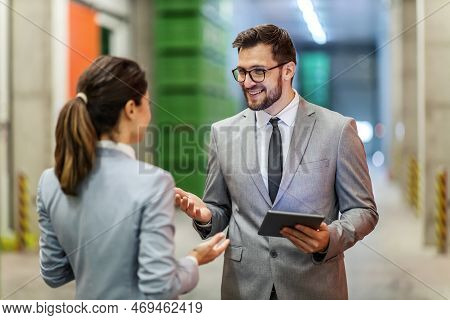 Warehouse Manager Training. A Man And A Woman In A Business Suit Stand In A Warehouse And Talk About