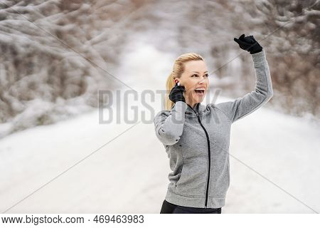 Happy Sportswoman Enjoying Music And Taking A Break From Exercising While Standing In Nature At Snow