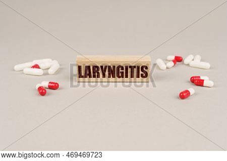 Medical Concept. On A Gray Surface Are Tablets, Capsules And A Wooden Plate With The Inscription - L