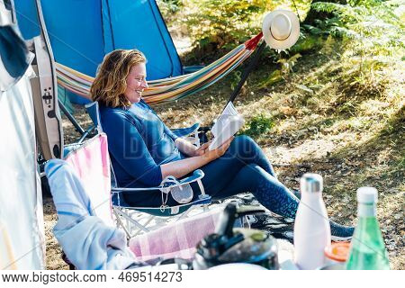 Adult Woman Relaxing, Sitting In The Travel Chair And Reading Book On The Background Of Camper Car V