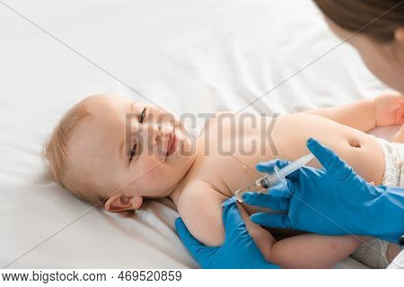 Doctor Vaccinating Smiling Baby In Clinic. One Year Little Baby Get An Injection. Pediatrician And P
