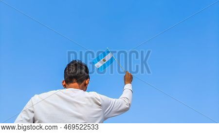 Boy Holding Argentina Flag Against Clear Blue Sky. Man Hand Waving Argentinian Flag View From Back, 