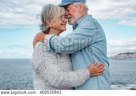 Happy Beautiful Senior Couple Tenderly Embracing By The Sea. Smiling Elderly Man And Woman Enjoying 