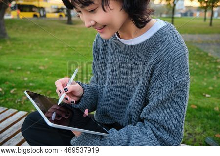 Portrait Of Young Smiling Korean Girl, Graphic Designer, Artist Drawing On Digital Tablet With A Pen