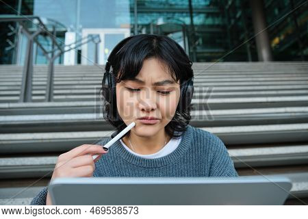 Portrait Of Asian Girl With Troubled Face, Draws On Digital Tablet With Pen, Looks Complicated At He