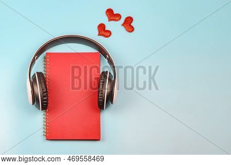 Top View Or Flat Lay Of Red Notebook Covered With Headphones On Blue Background Decorated With Red G