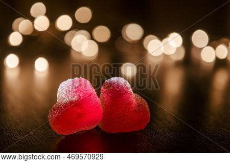Two Red Sugar Marmalade Candies In Shape Of Heart On Black Background, Lit From Side, Behind Round Y